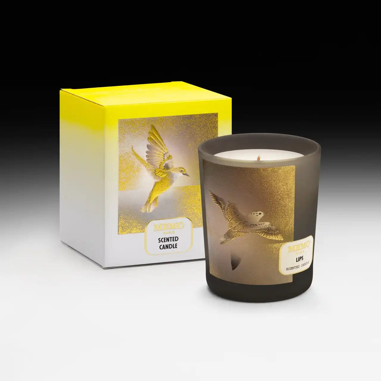 A yellow and white boxed scented candle with a matching candle in a frosted glass holder, both featuring a gold bird design.