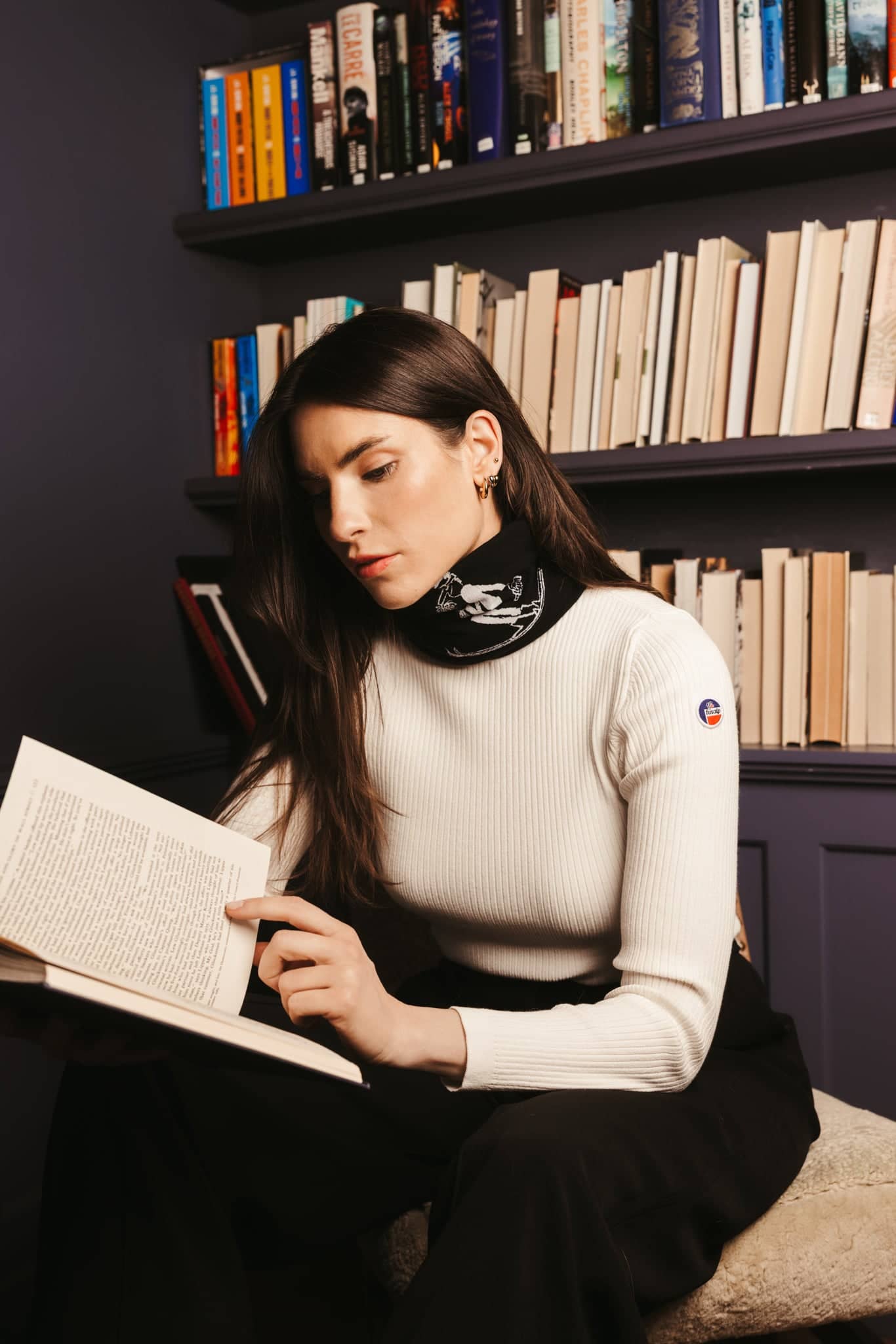 White ribbed knit sweater with black high neck collar featuring a white embroidered design and a small circular logo on the sleeve.